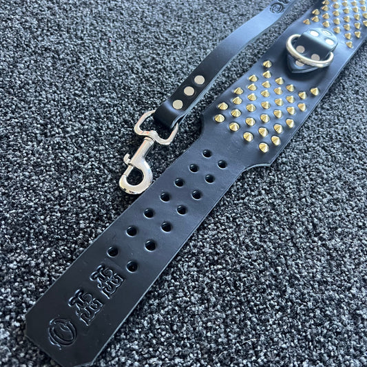 Black leather dog leash with gold studs and metal clasp on a textured gray surface