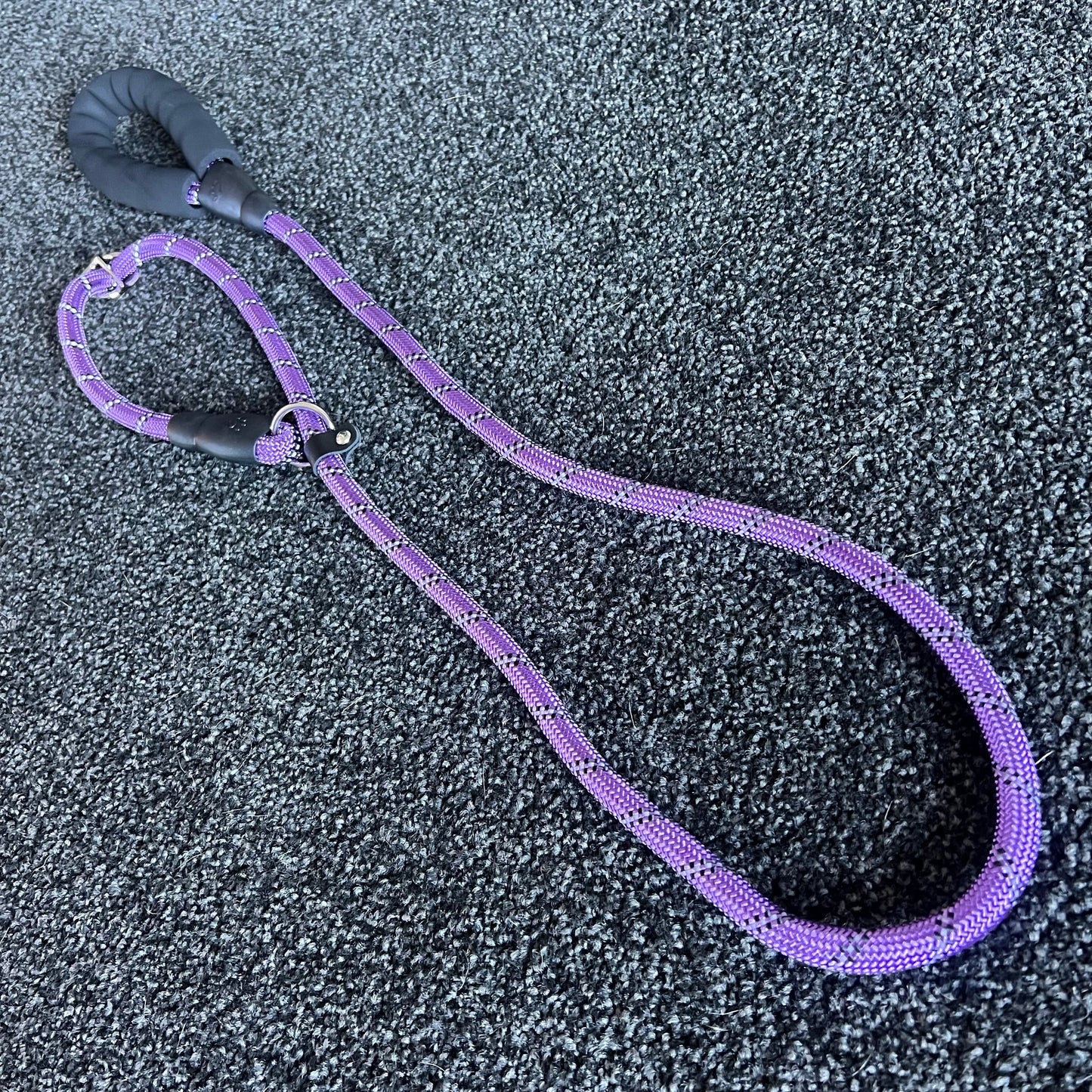 Purple dog leash with black handle on a textured gray surface