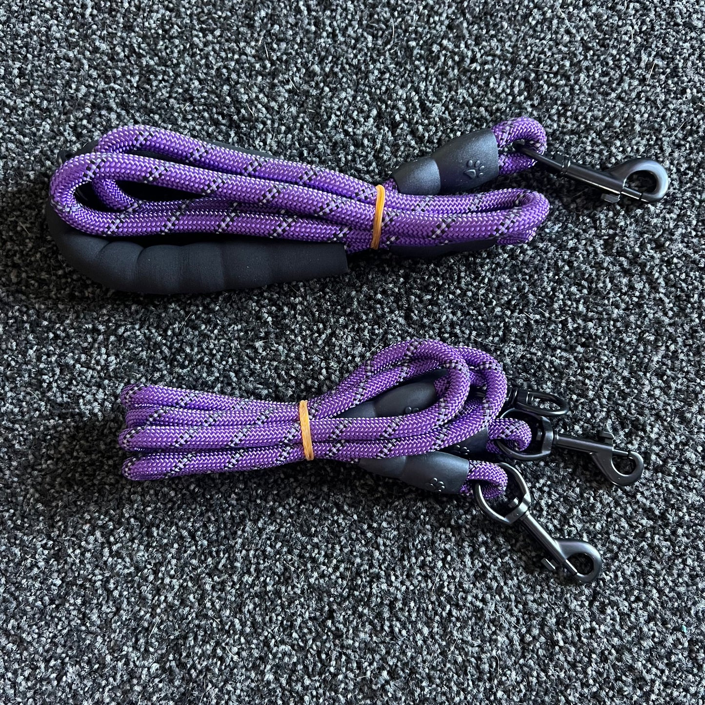 Two purple dog leashes with black handles on a gray textured surface