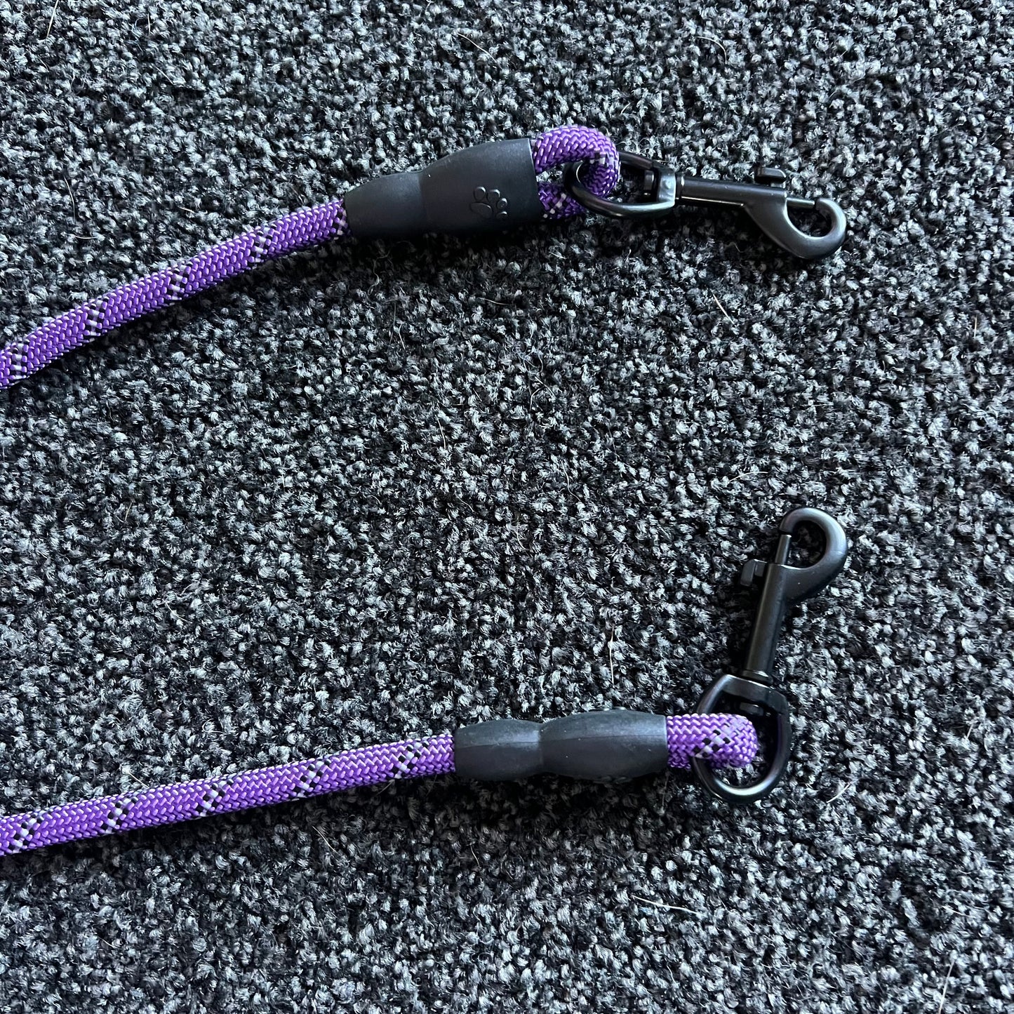 Two purple and black dog leashes on a textured gray surface