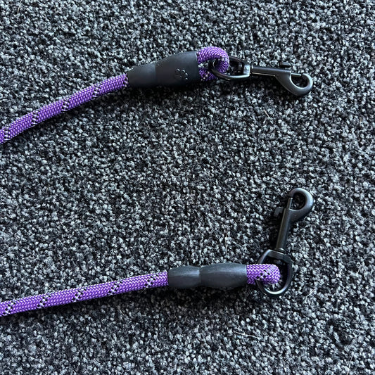 Two purple and black dog leashes on a textured gray surface