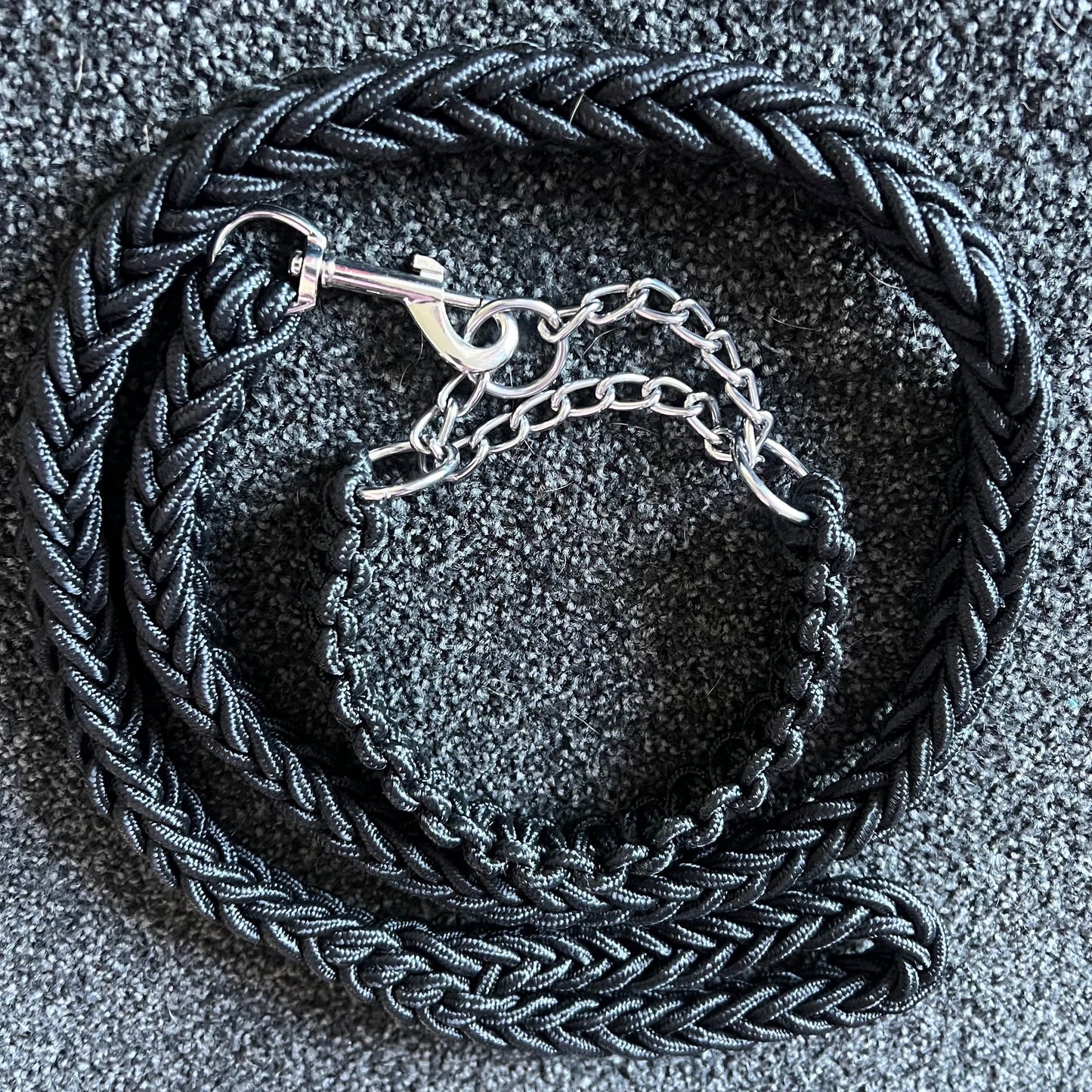 Black braided leather leash with a silver clasp on a textured gray surface