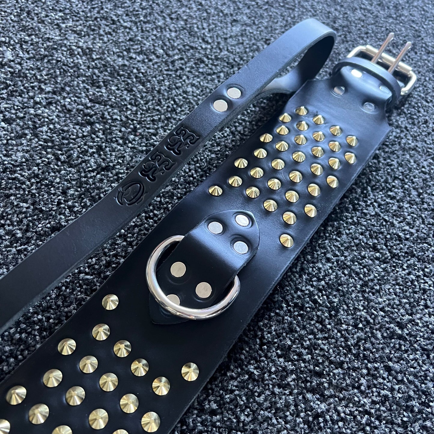 Black leather strap with gold studs on a textured black background