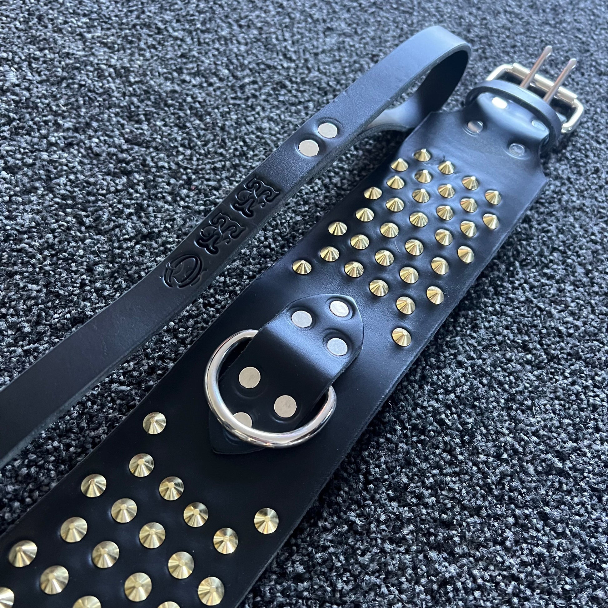 Black leather strap with gold studs on a textured black background