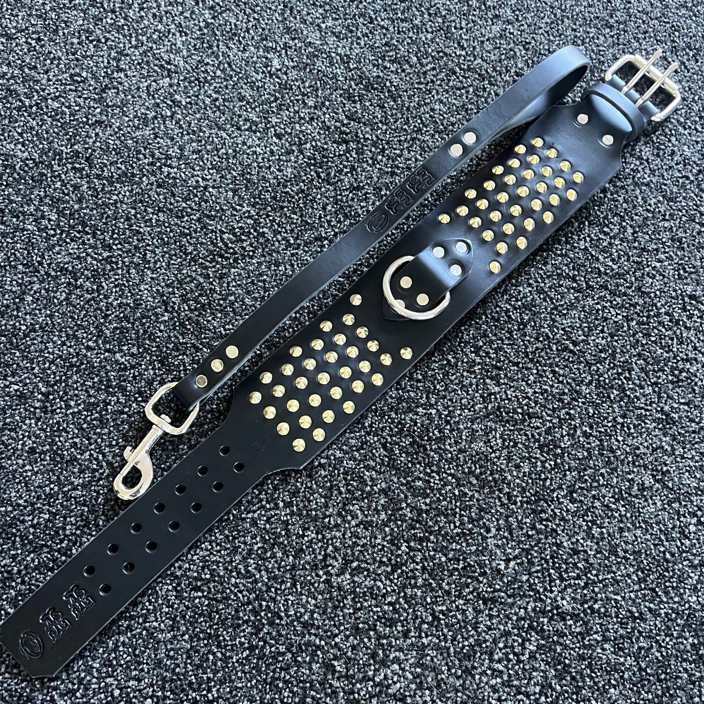 Black leather strap with gold studs and a smiley face design on a textured black background