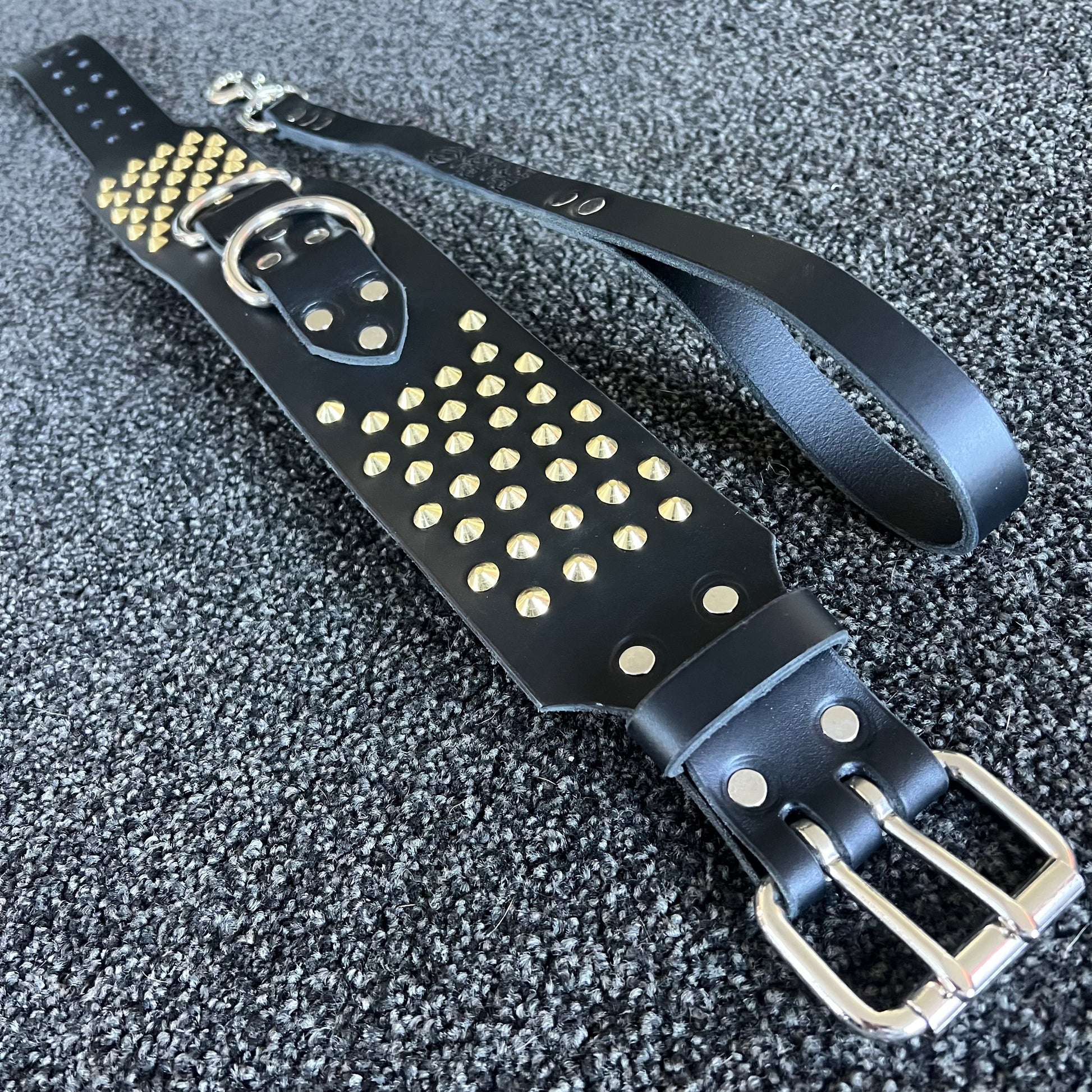 Black leather belt with gold studs and silver buckle on a textured black background