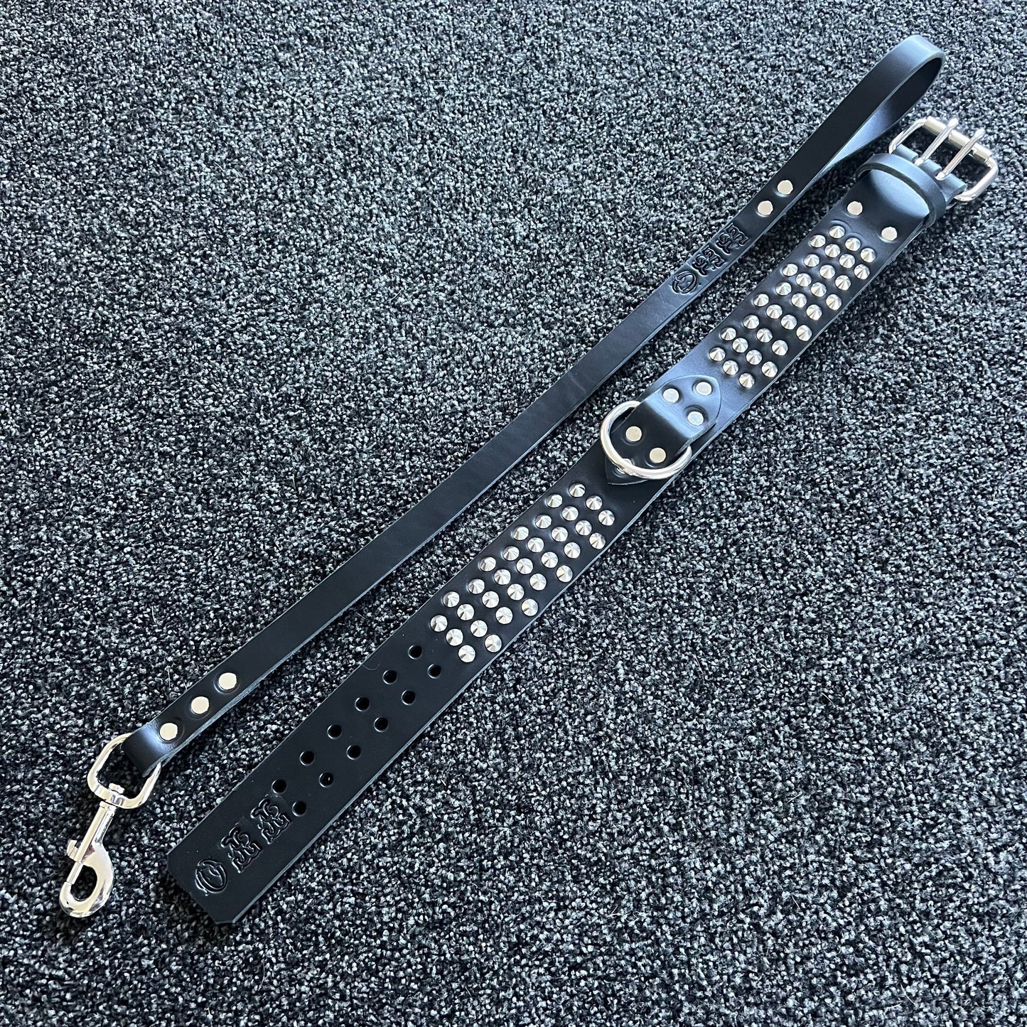 Black leather strap with silver studs and hardware on a textured gray surface