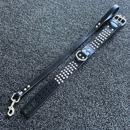 Black leather strap with silver studs and hardware on a textured gray surface