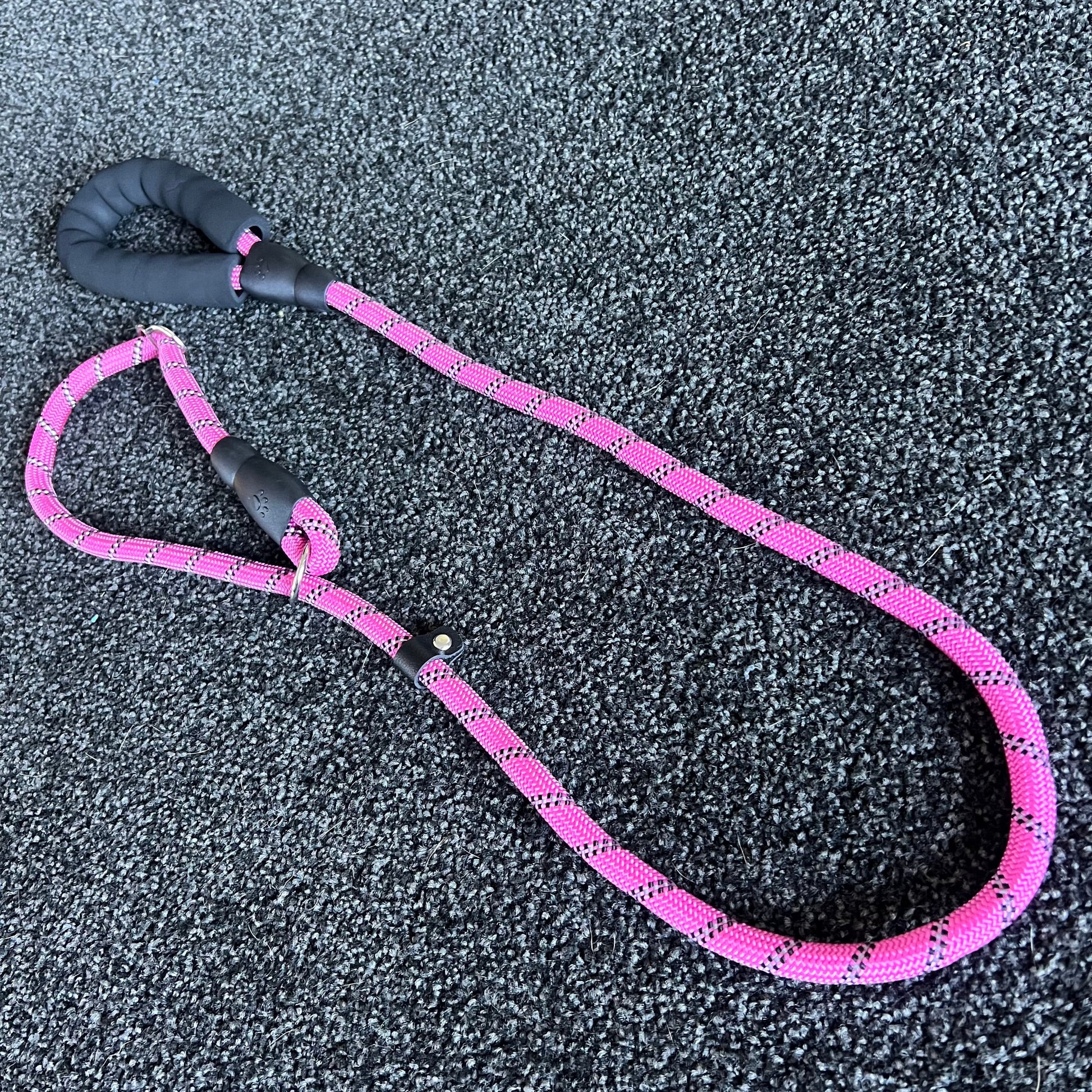 Pink dog leash with black handle on a textured gray surface