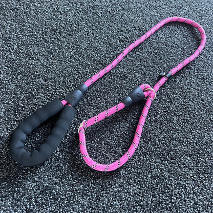 Pink dog leash with black handle on a textured gray surface