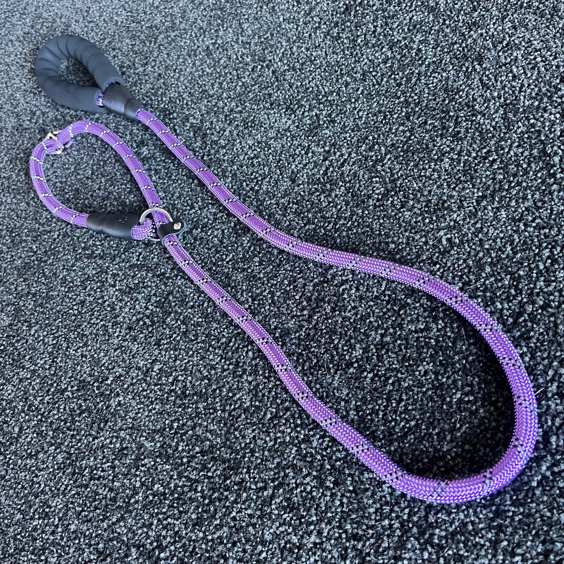 Purple dog leash with black handle on a textured gray surface