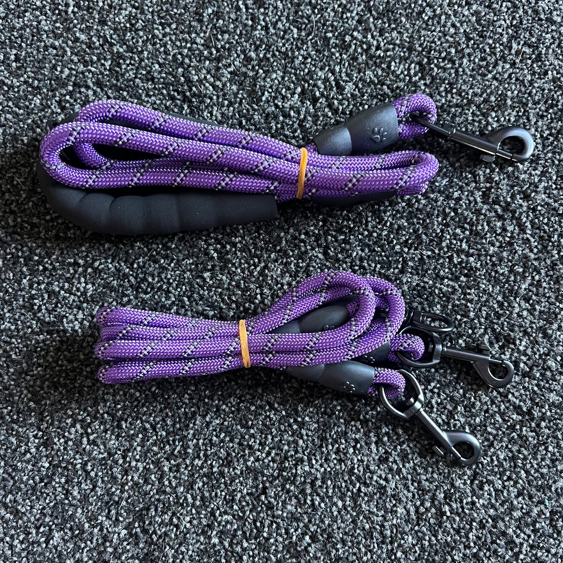 Two purple dog leashes with black handles on a gray textured surface