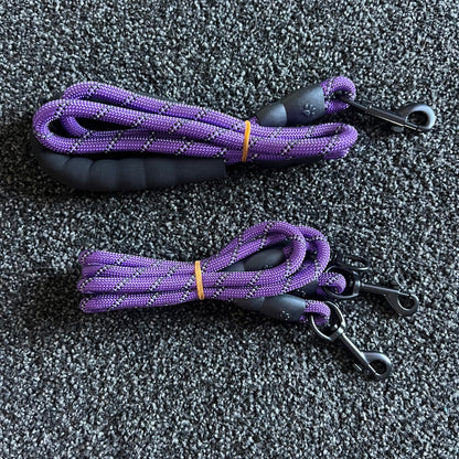 Two purple dog leashes with black handles on a gray textured surface