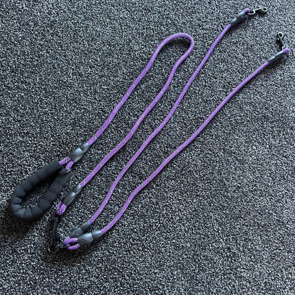 Purple dog leash with black handles on a dark textured surface