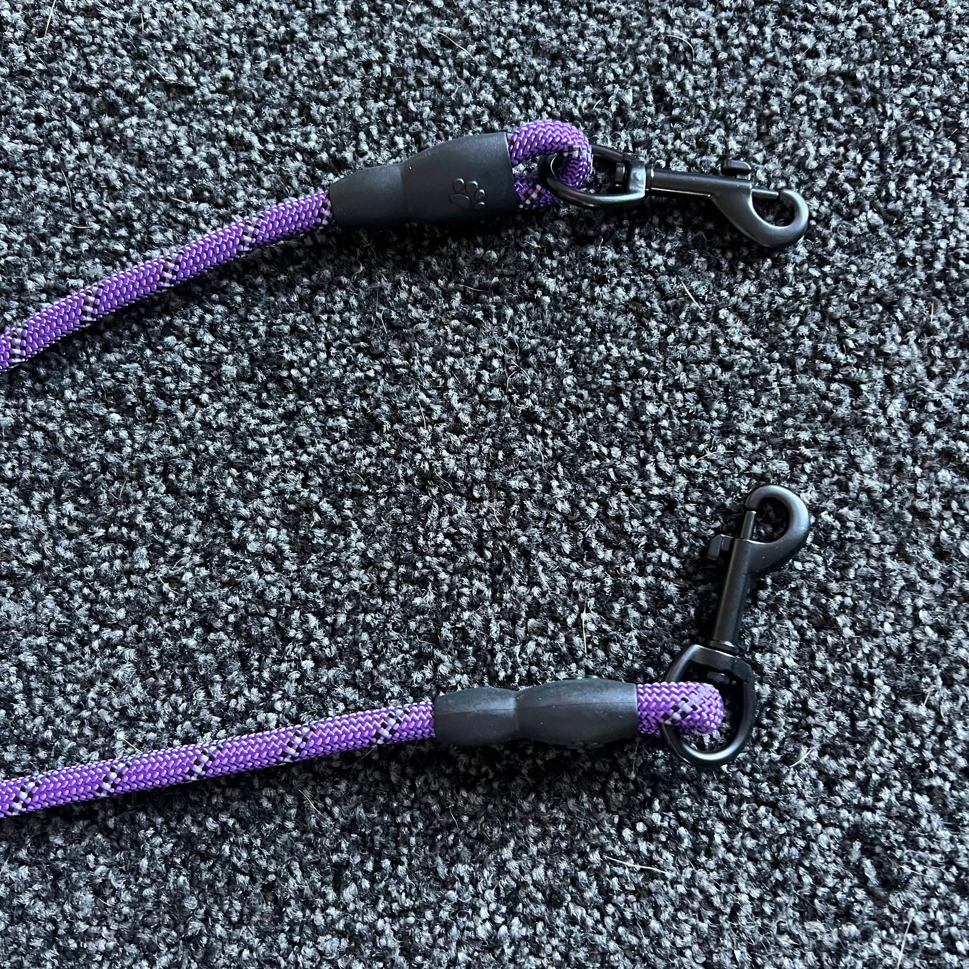 Two purple and black dog leashes on a textured gray surface