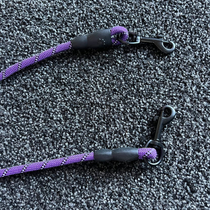 Two purple and black dog leashes on a textured gray surface