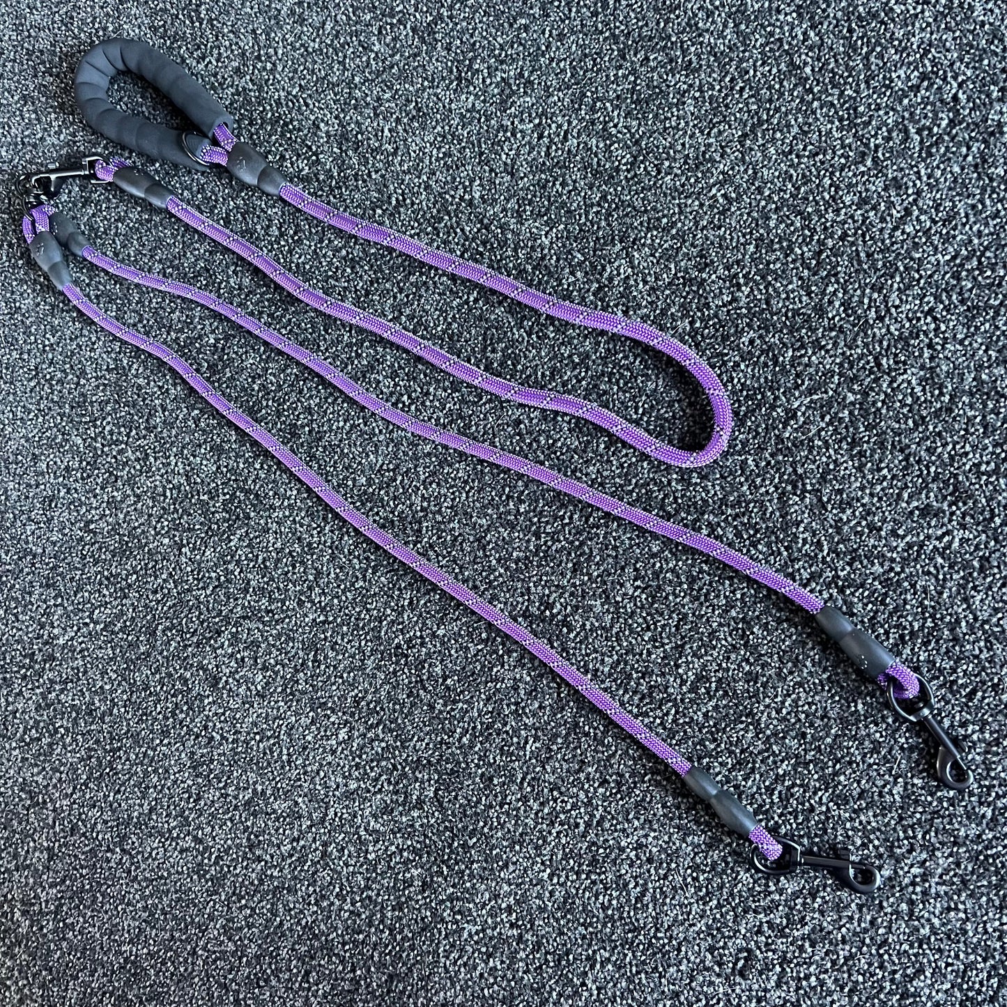 Purple dog leash with black handles on a textured gray surface
