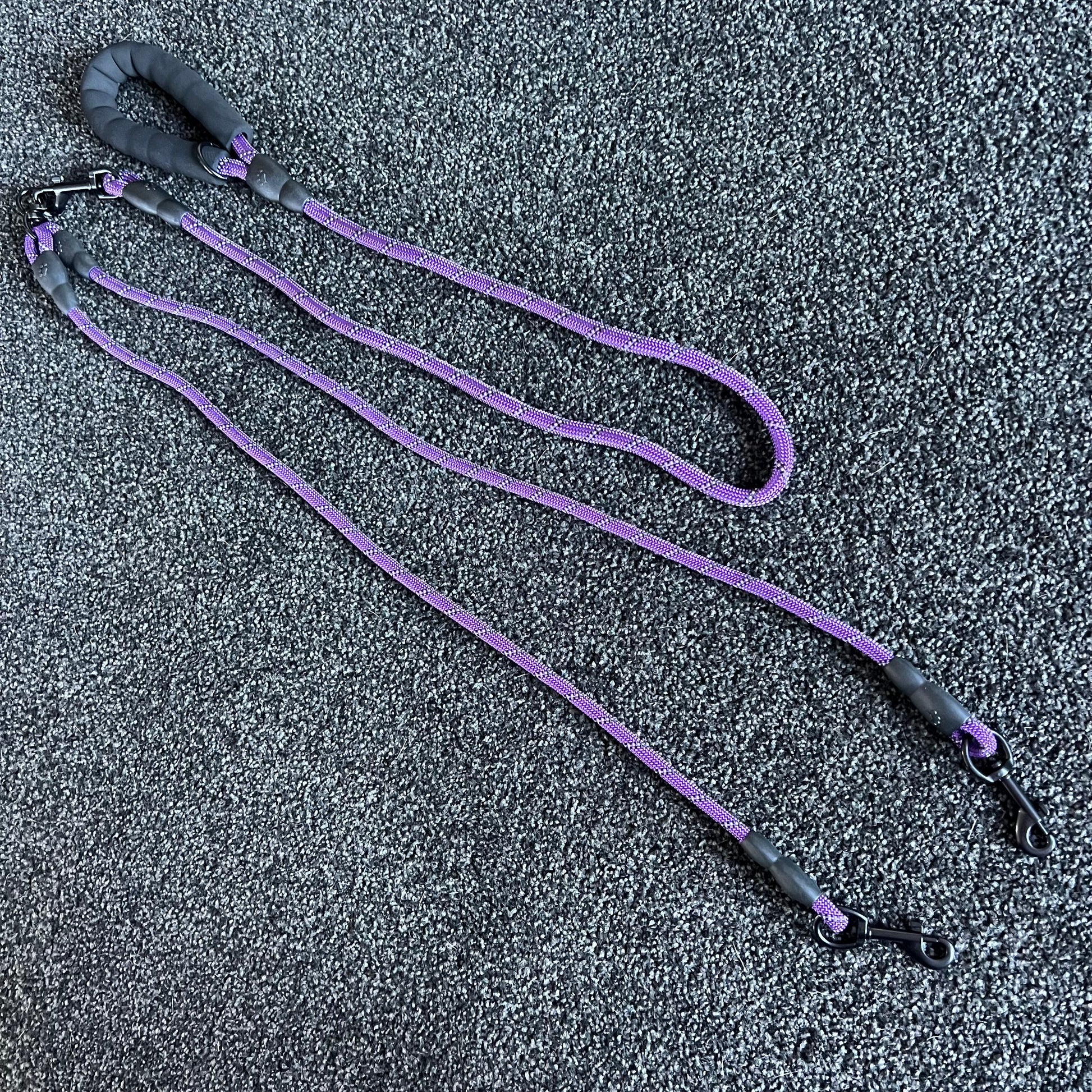 Purple dog leash with black handles on a textured gray surface