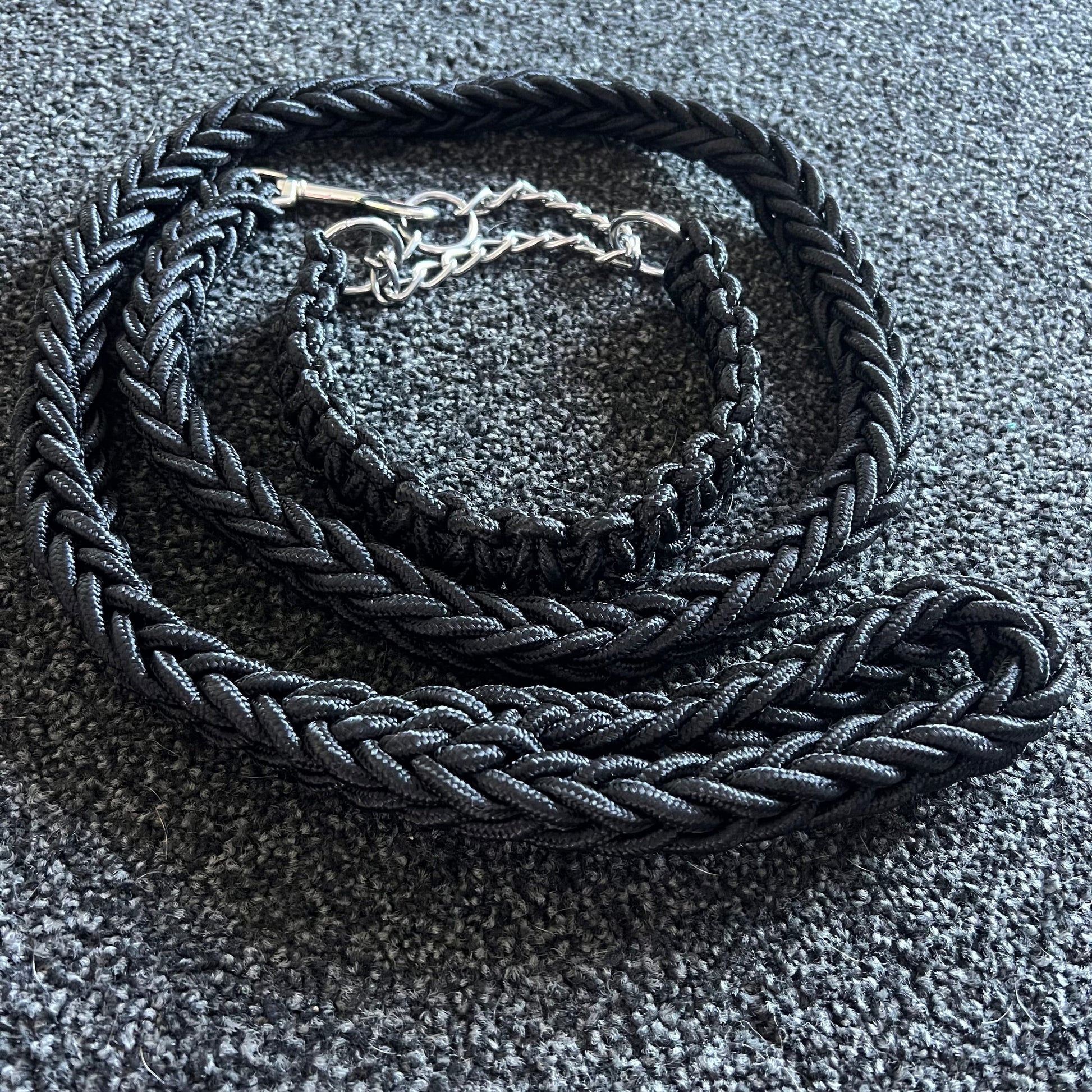 Black braided dog collar with a silver buckle on a textured gray surface